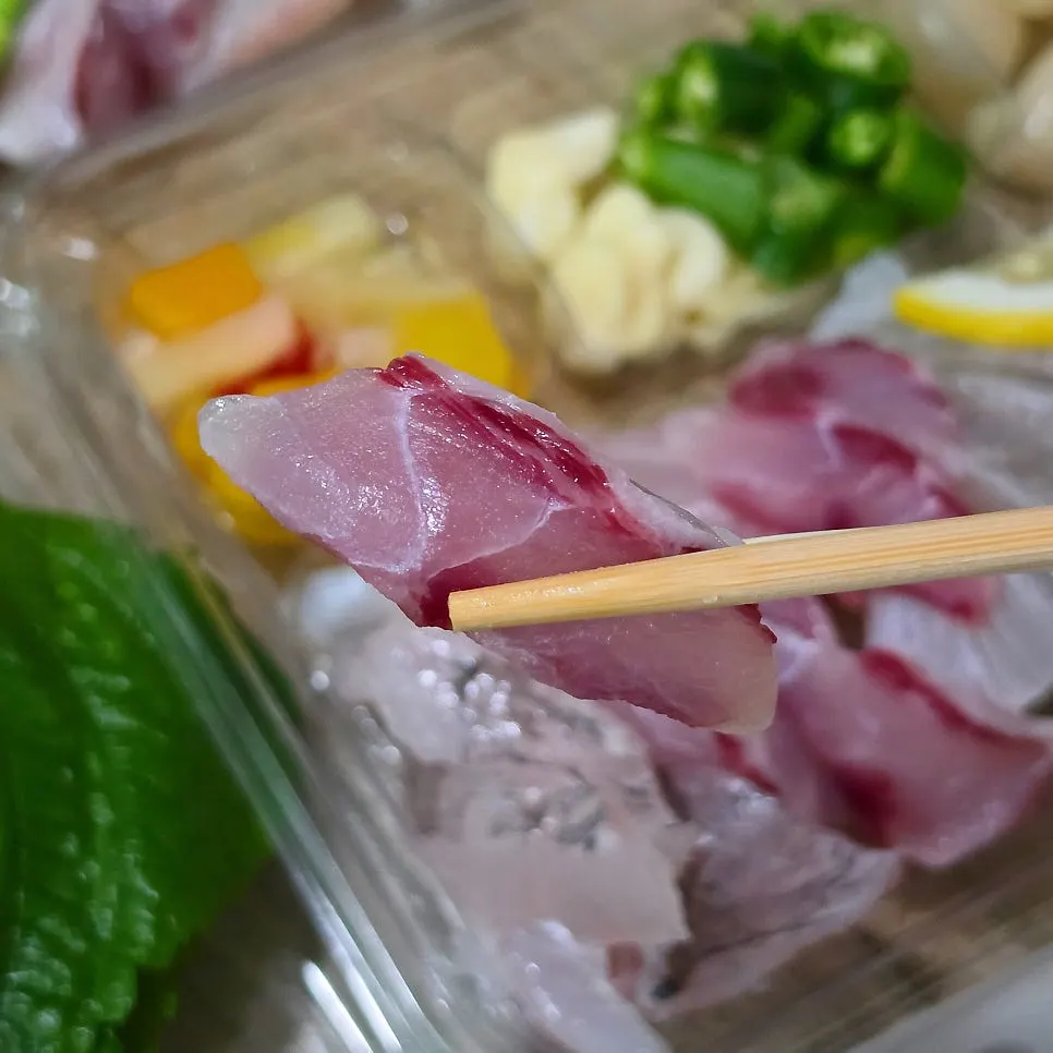 A single piece of sashimi lifted with chopsticks