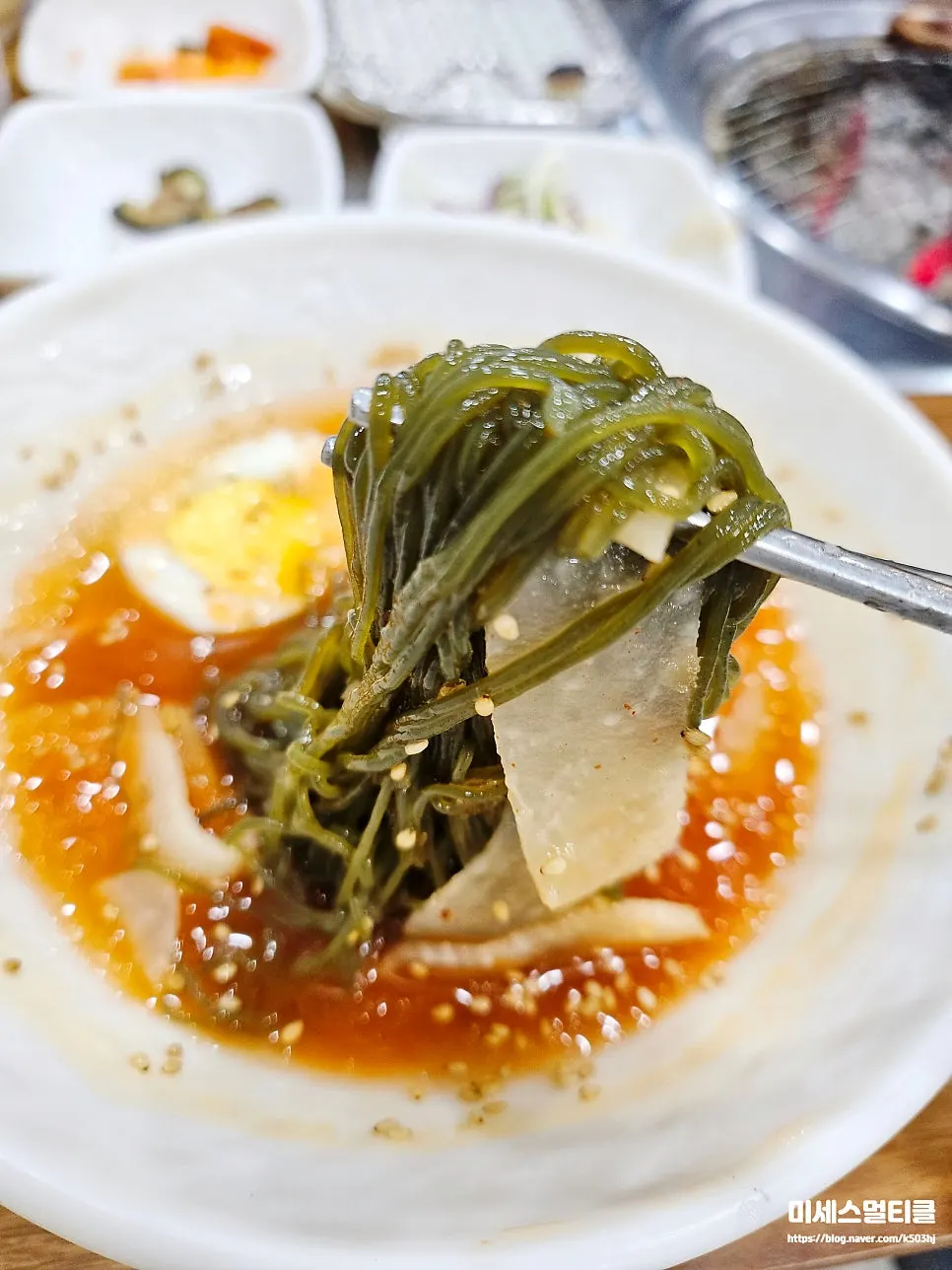 Vertical photo of naengmyeon noodles lifted with chopsticks