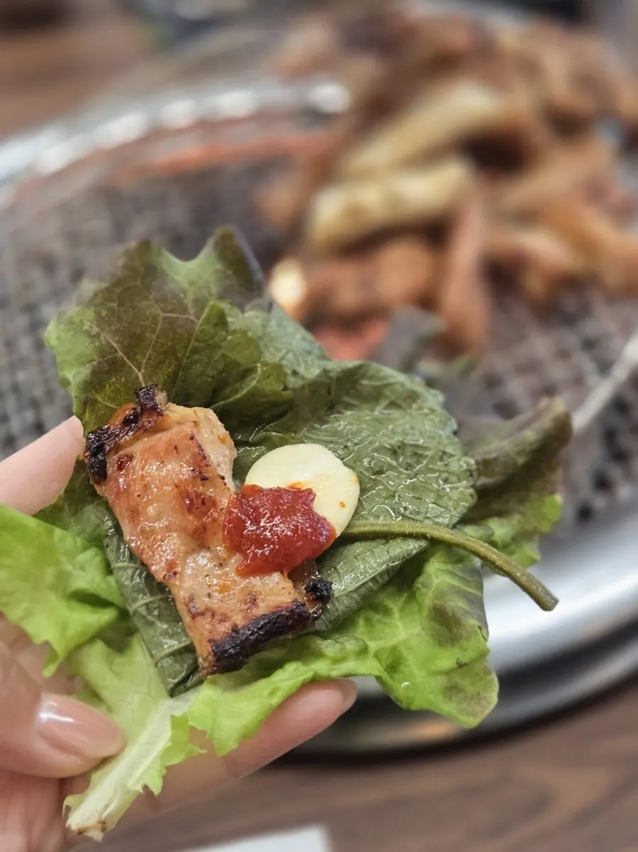 Dakgalbi wrap with lettuce, perilla leaf, and garlic