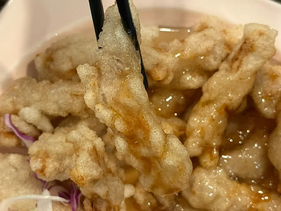 A piece of sweet and sour pork lifted with chopsticks