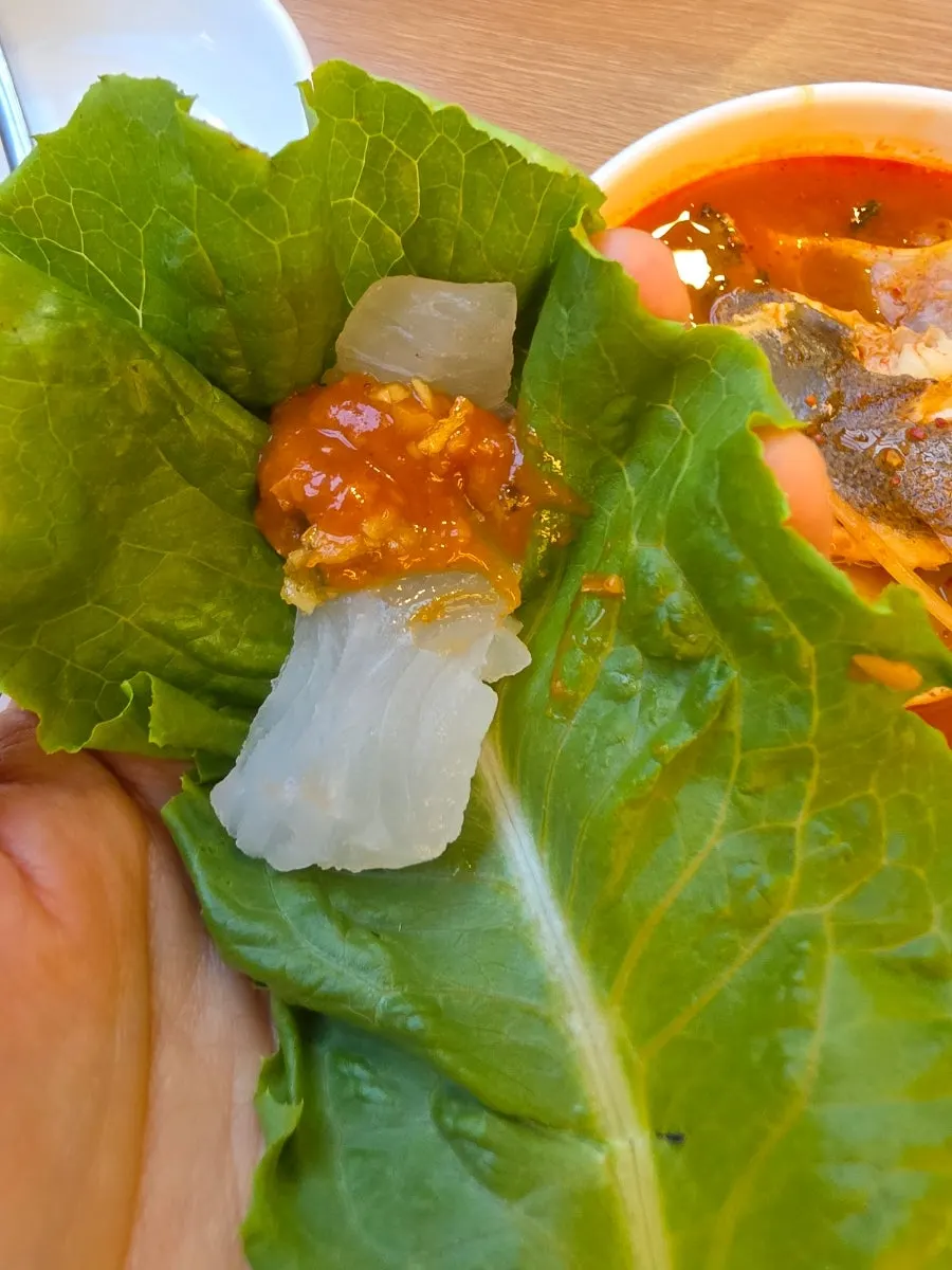 A piece of halibut sashimi lifted with chopsticks