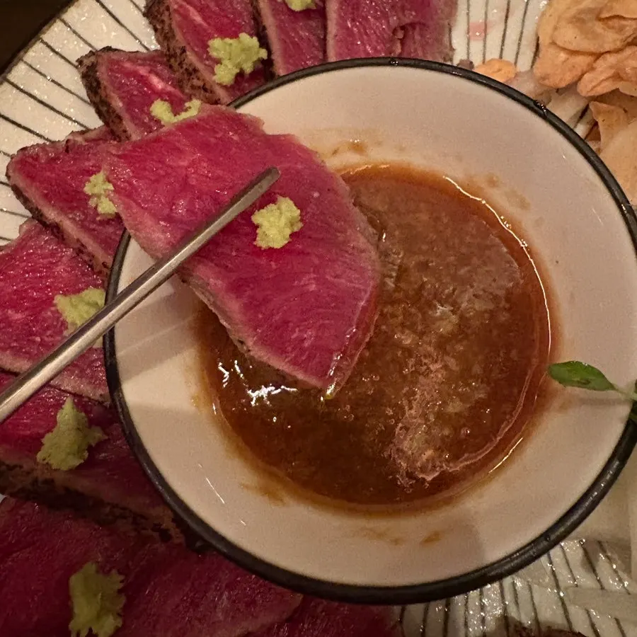 A piece of beef tataki dipped in sauce
