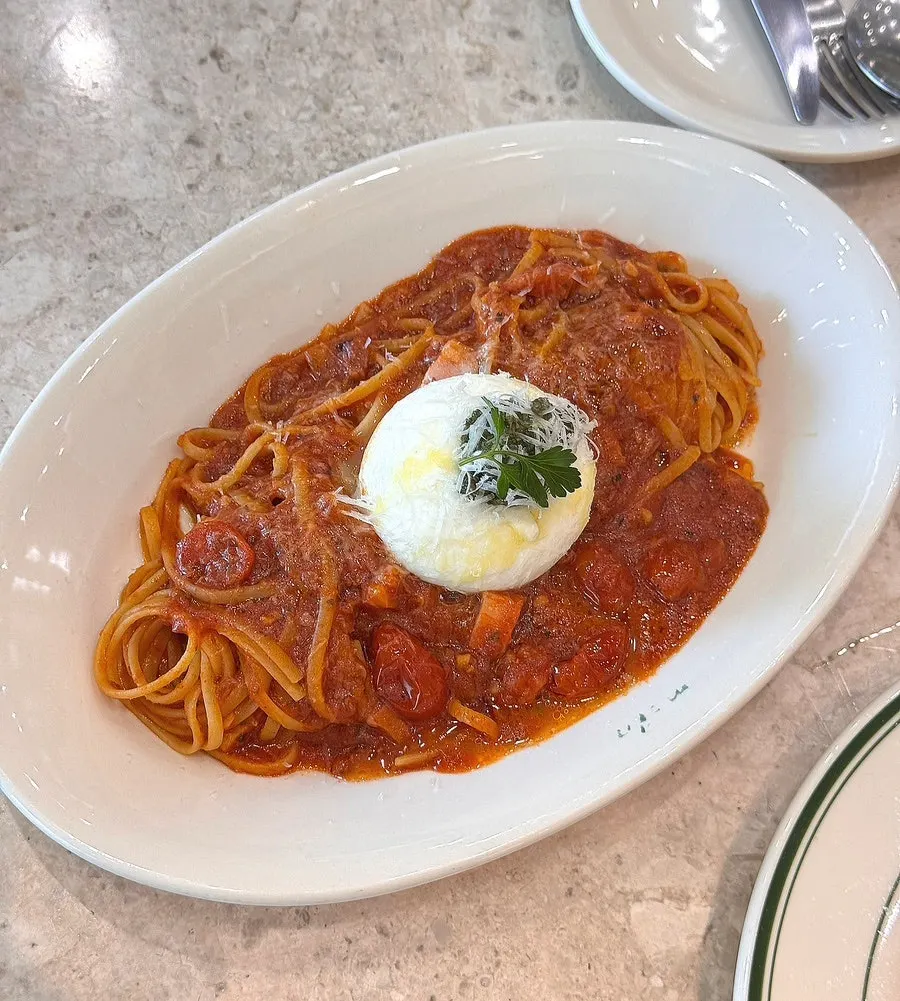 A whole burrata cheese ball on top of the pasta