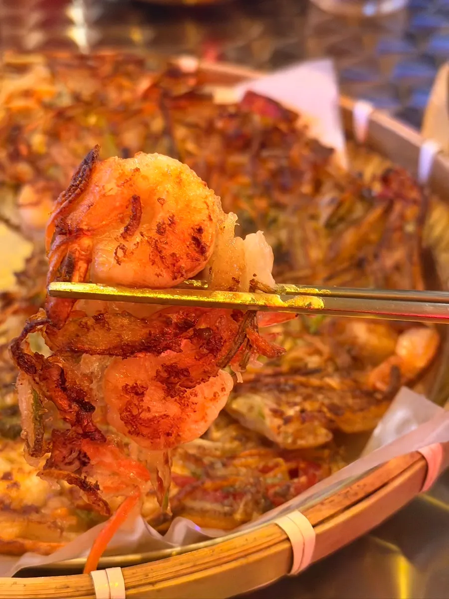 A piece of squid-shrimp pancake held with chopsticks