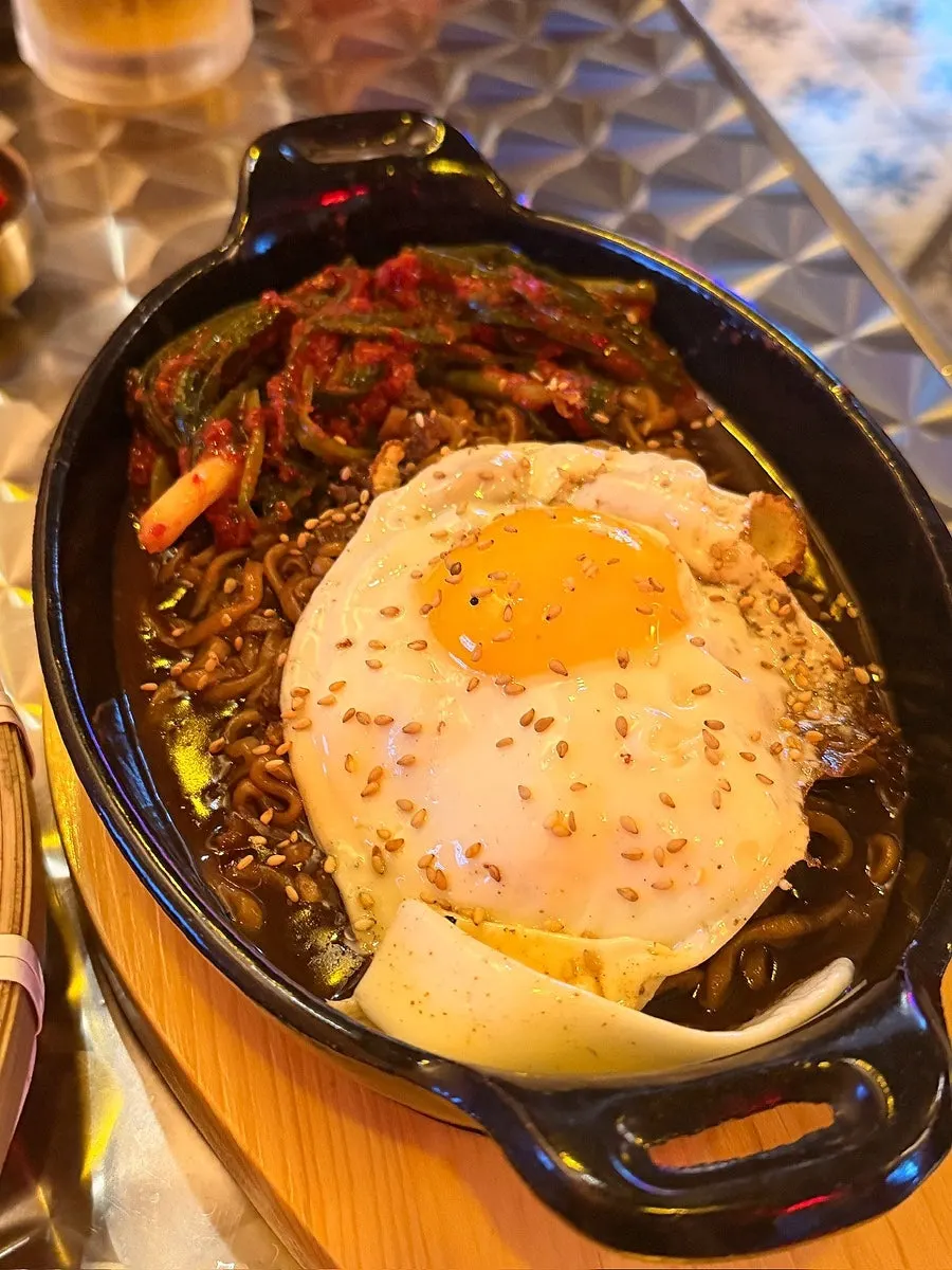 Jjapaguri and green onion kimchi served on a hot stone plate