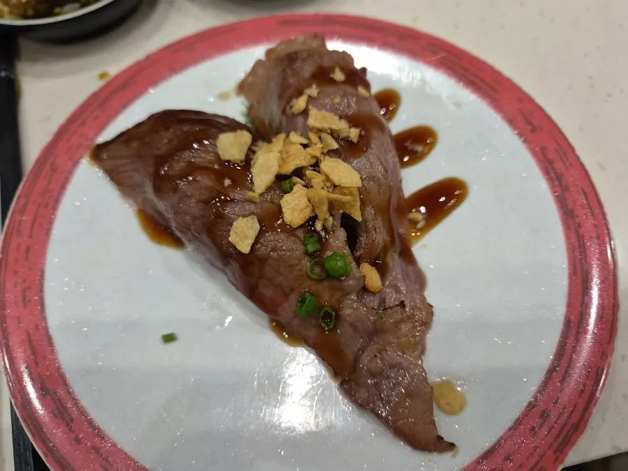 A plate of beef tartare sushi with the conveyor belt in view