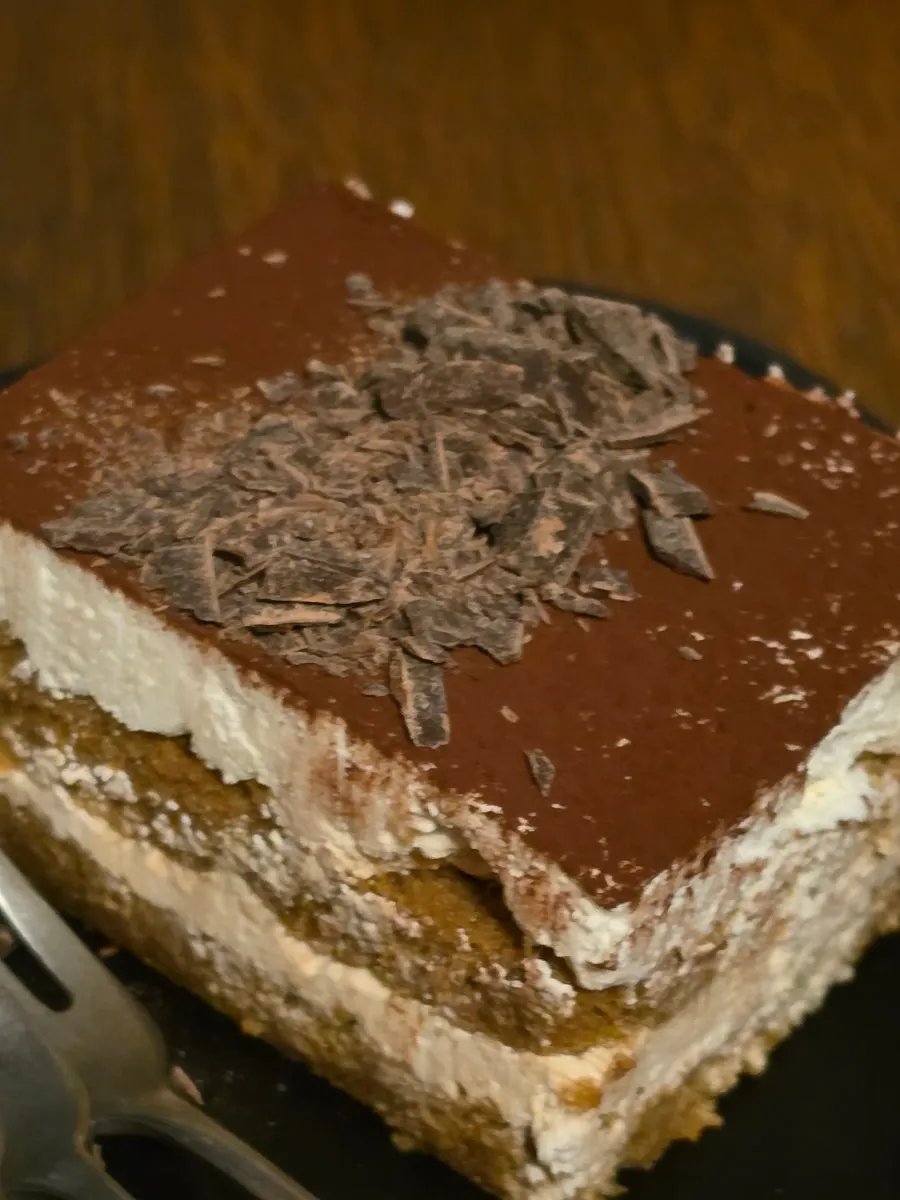 A large slice of tiramisu topped with cocoa powder