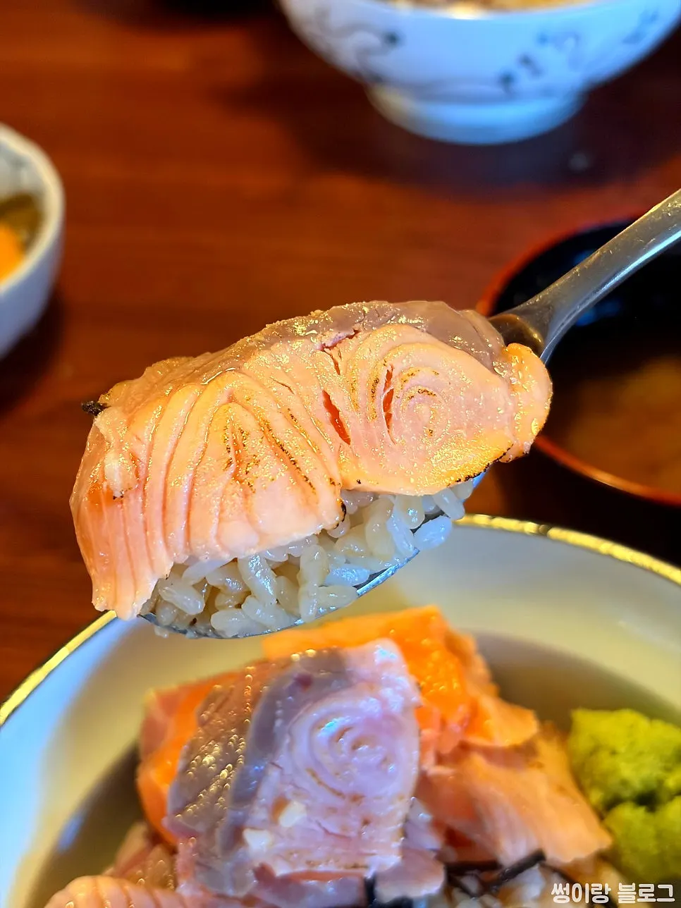Chopsticks picking up a piece of salmon from the abburi sake-don