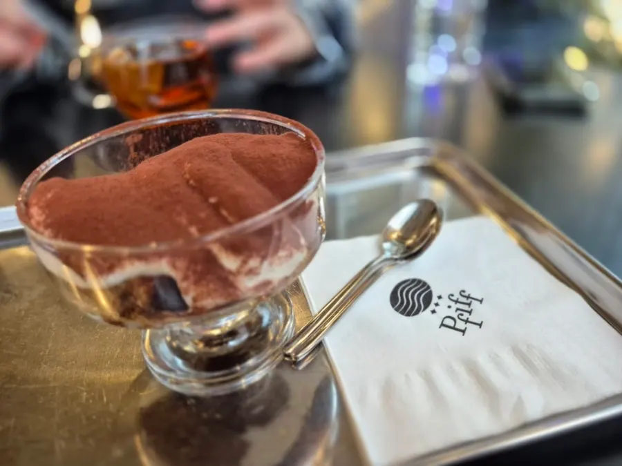 A cross-section of the tiramisu next to a cup of coffee