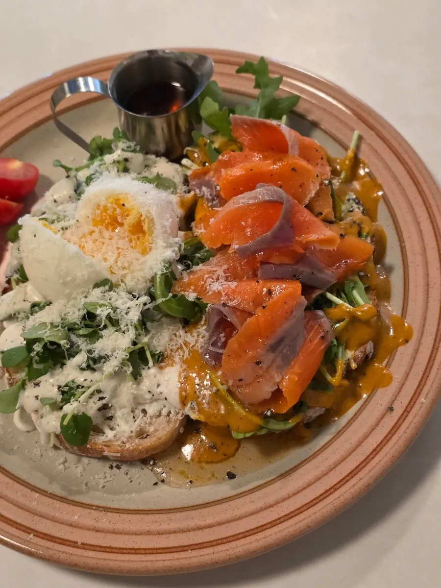 Salmon sandwich topped with rugola, soft-boiled egg, and tomato