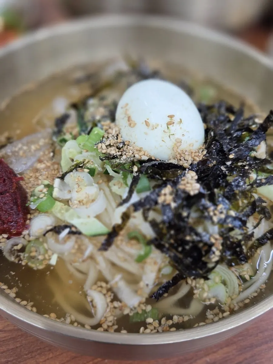 Close-up of cold kalguksu topped with seaweed flakes and cucumber