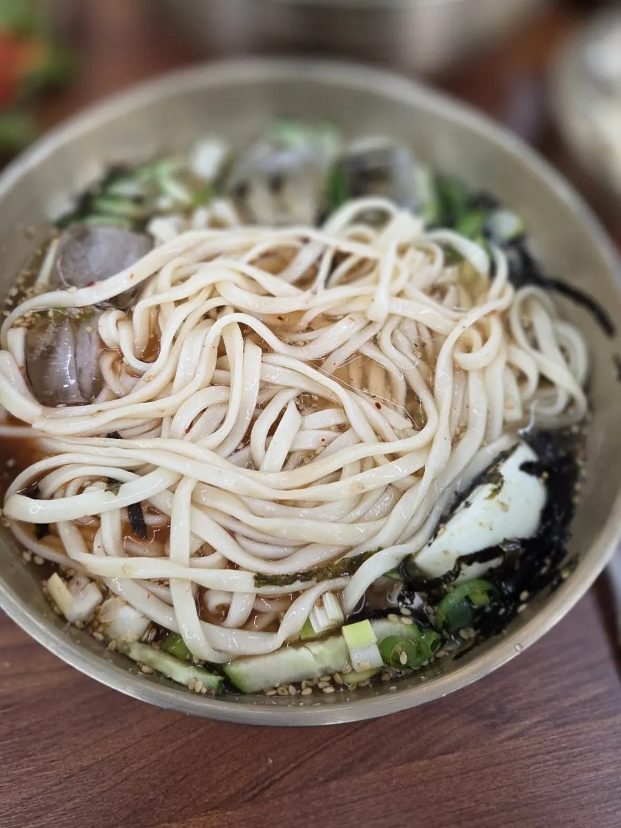 Chopsticks lifting cold kalguksu noodles from the bowl