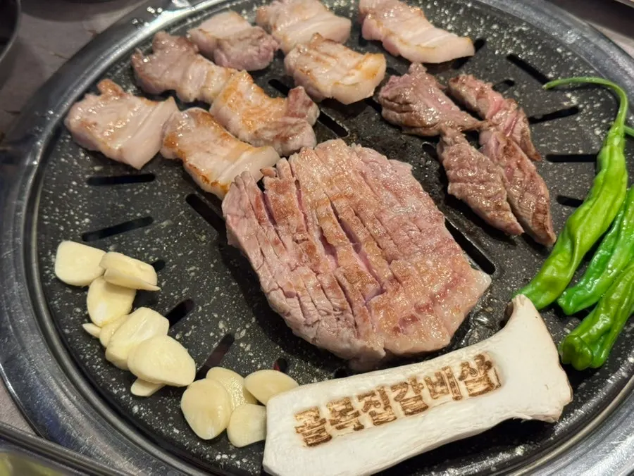 불판에서 익어가는 모둠 고기와 마늘, 고추