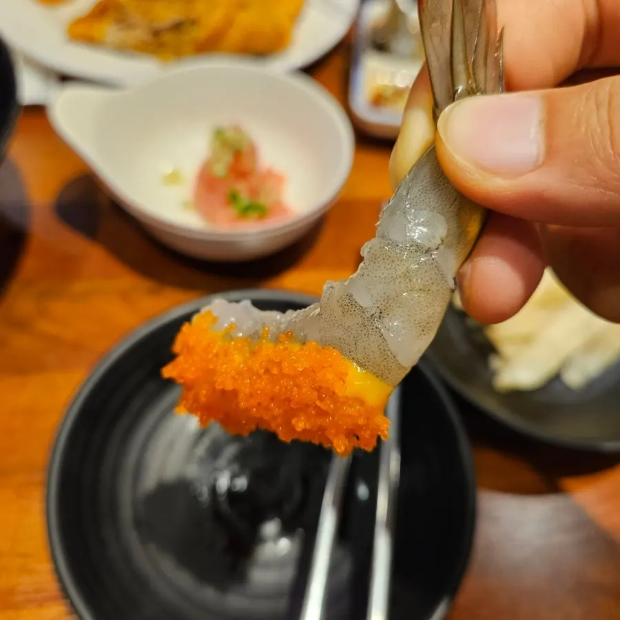 Piece of raw shrimp sashimi with flying fish roe clinging on