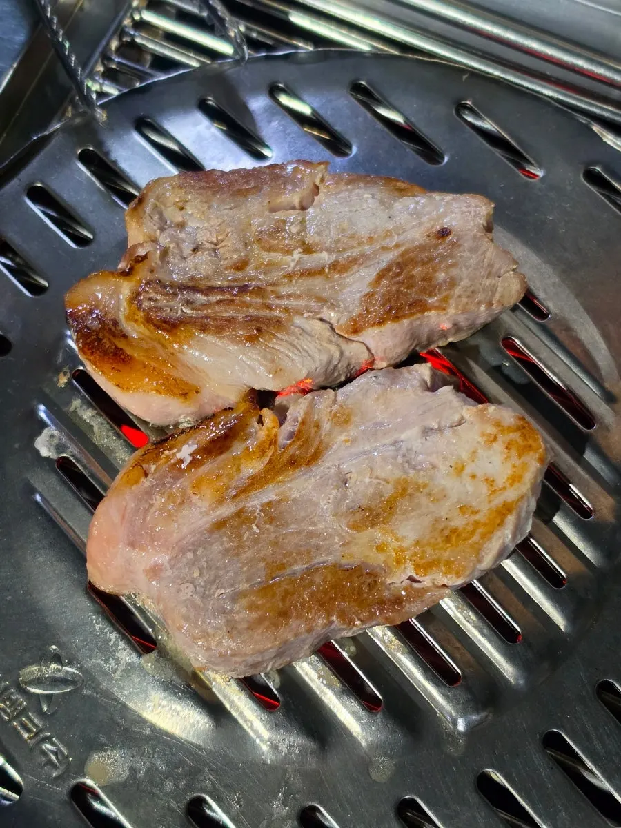 Thick pork neck grilling over charcoal