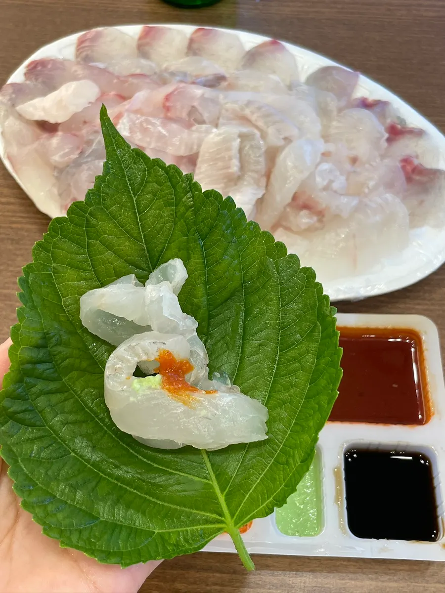 A bite of sashimi wrapped in perilla leaf