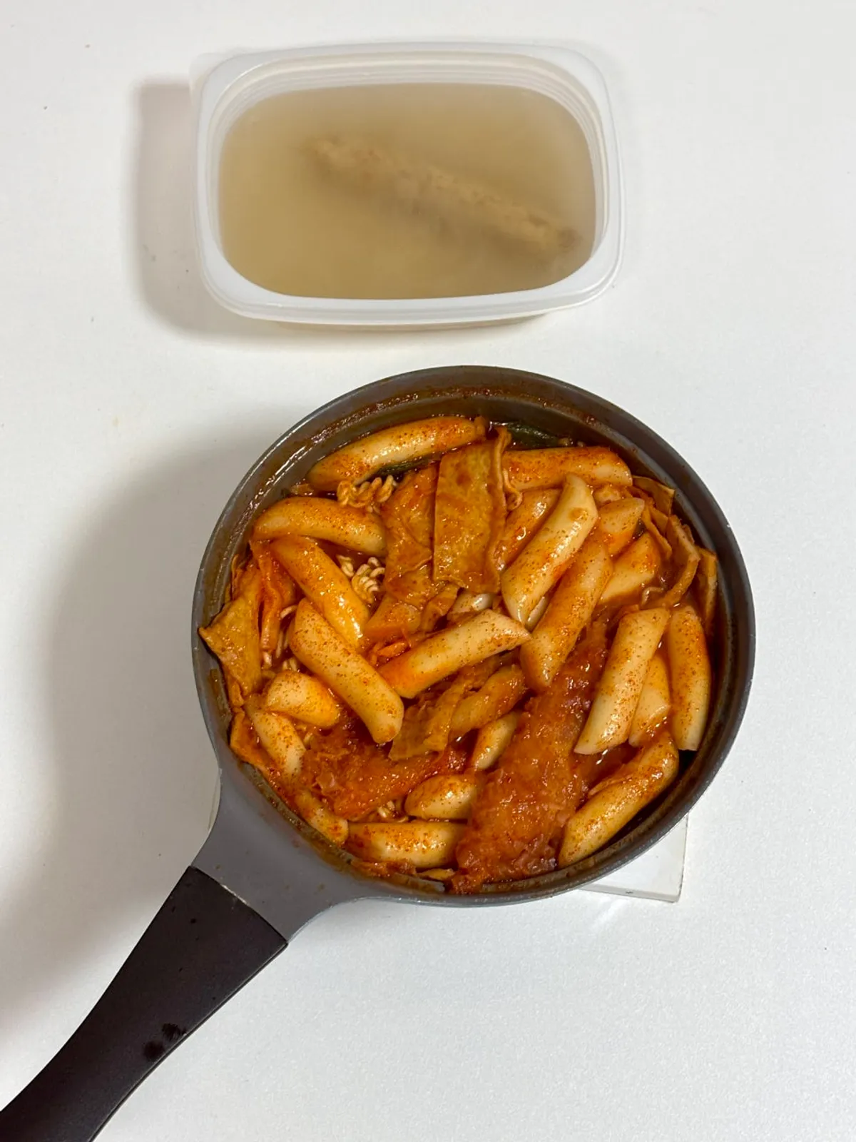 Adding vegetables, rice cakes, and ramen noodles to the boiling sauce and stirring