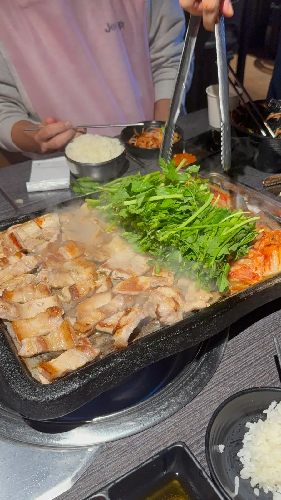 A piece of pork belly topped with minari and grilled kimchi