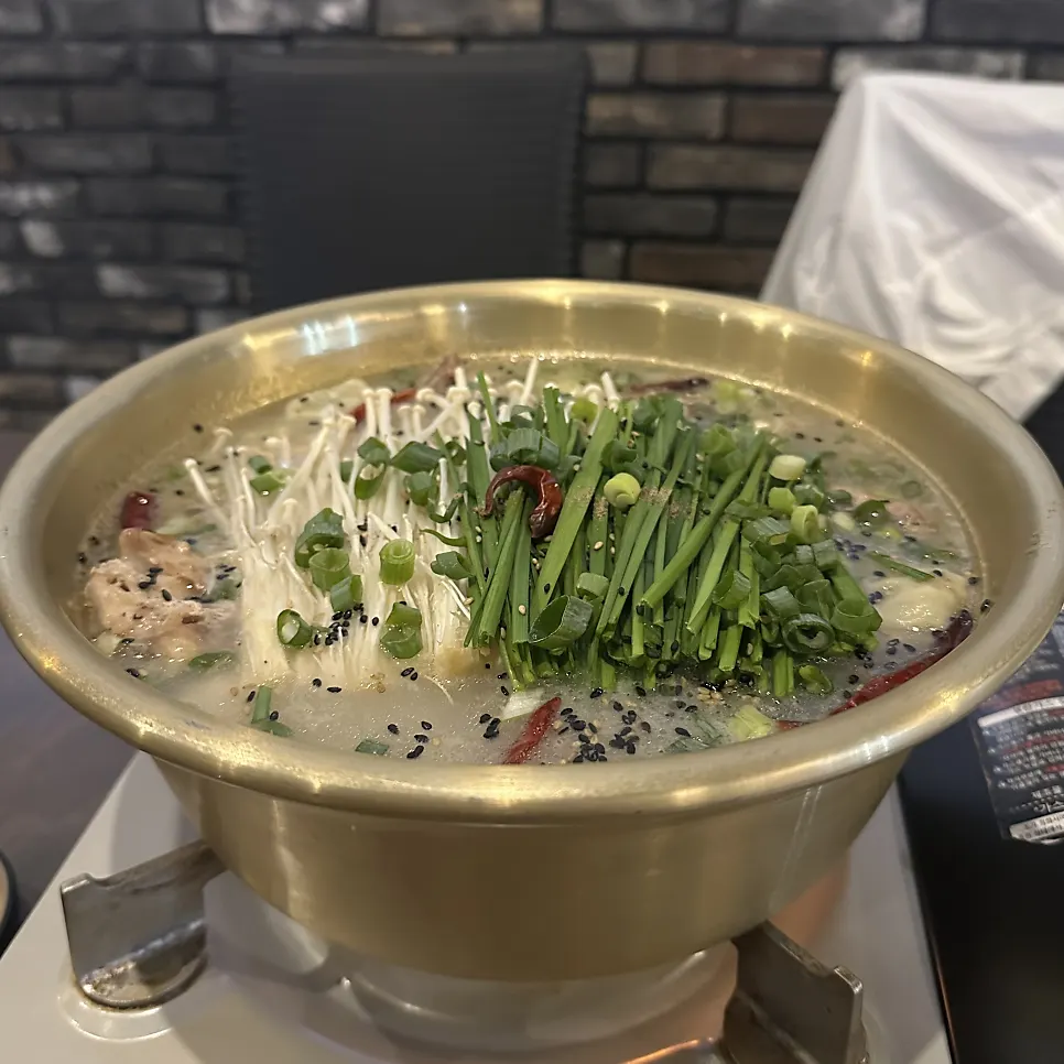 Pot of herbal dak han mari topped with chives and enoki mushrooms