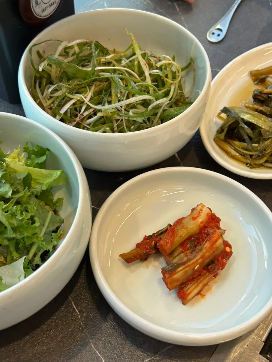 A plate of lettuce wraps, seasoned scallions, seasoned young cabbage, and mustard leaf kimchi