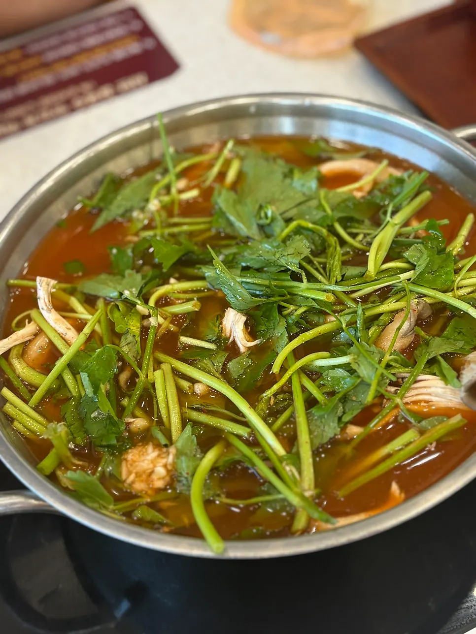 Pot of spicy shabu broth loaded with mushrooms and minari