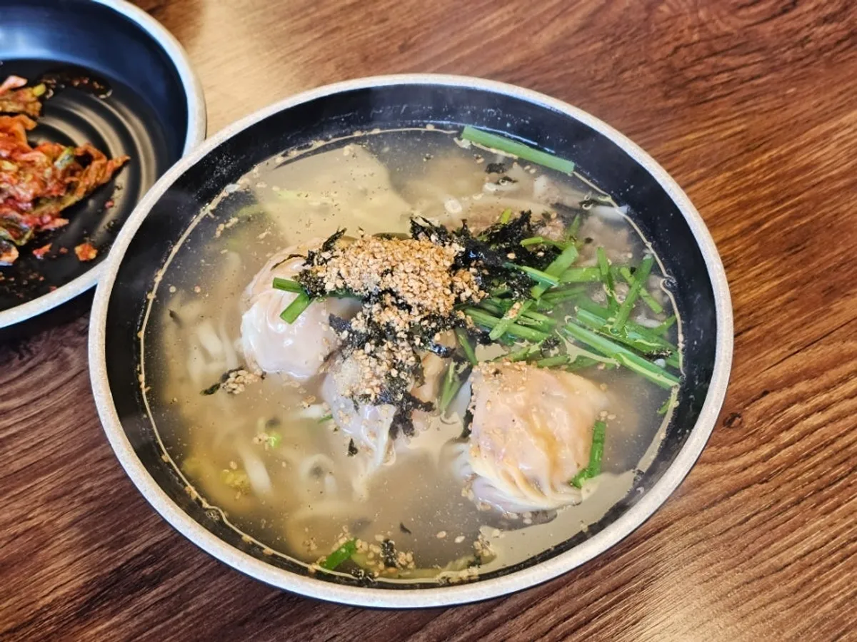Bowl of kalmandu-guk topped with seaweed flakes and chives