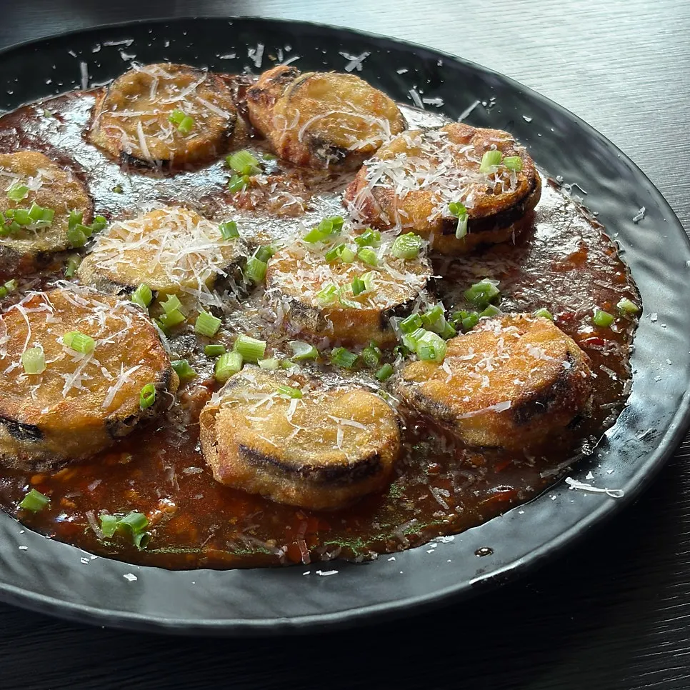 Chopsticks lifting a piece of the fish-tank eggplant fritters