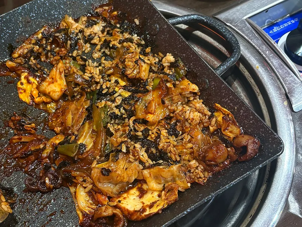Fried rice being stir-fried in leftover sauce on the griddle