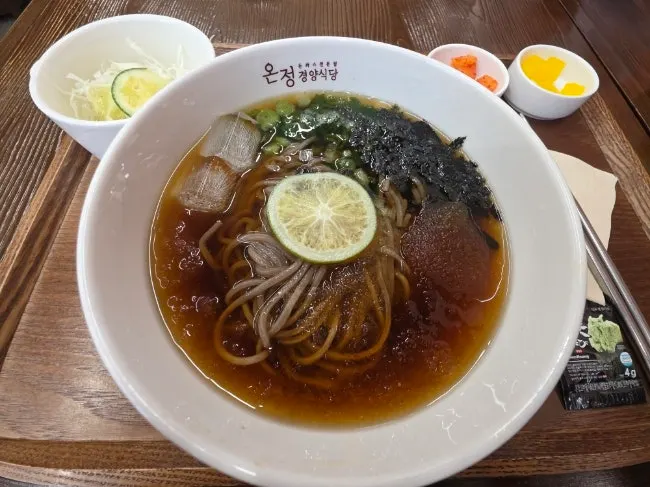 Green tangerine cold soba with dried seaweed flakes on icy broth