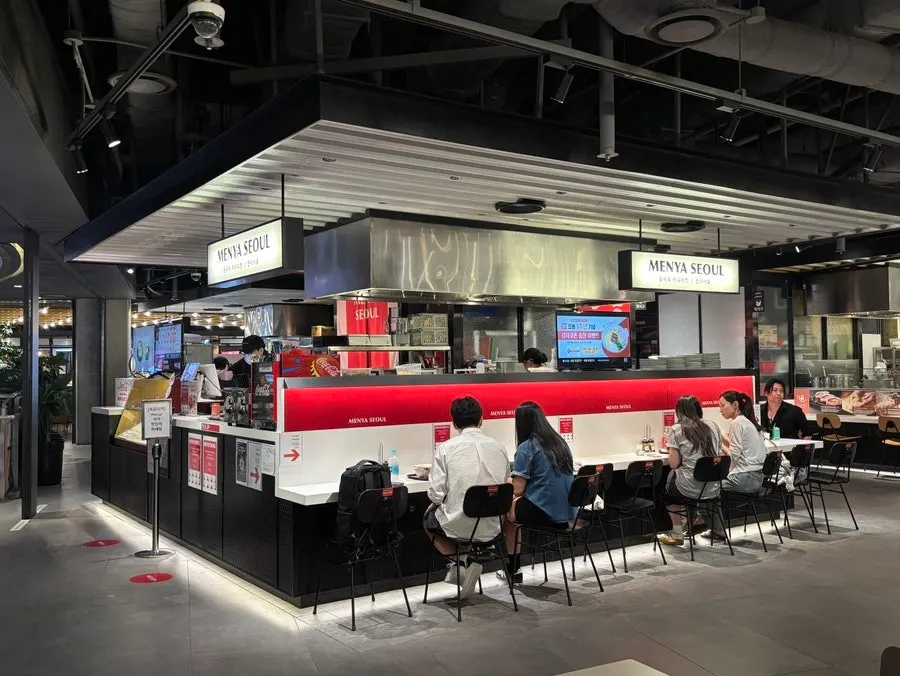 Shared tables and bar seats in front of Menya Seoul
