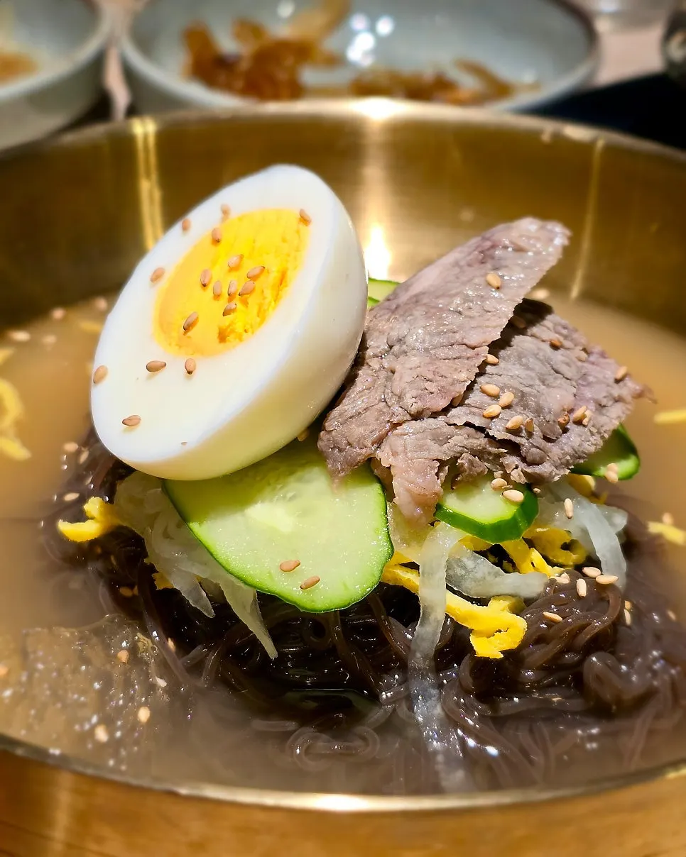 Mul naengmyeon topped with meat, egg, and cucumber