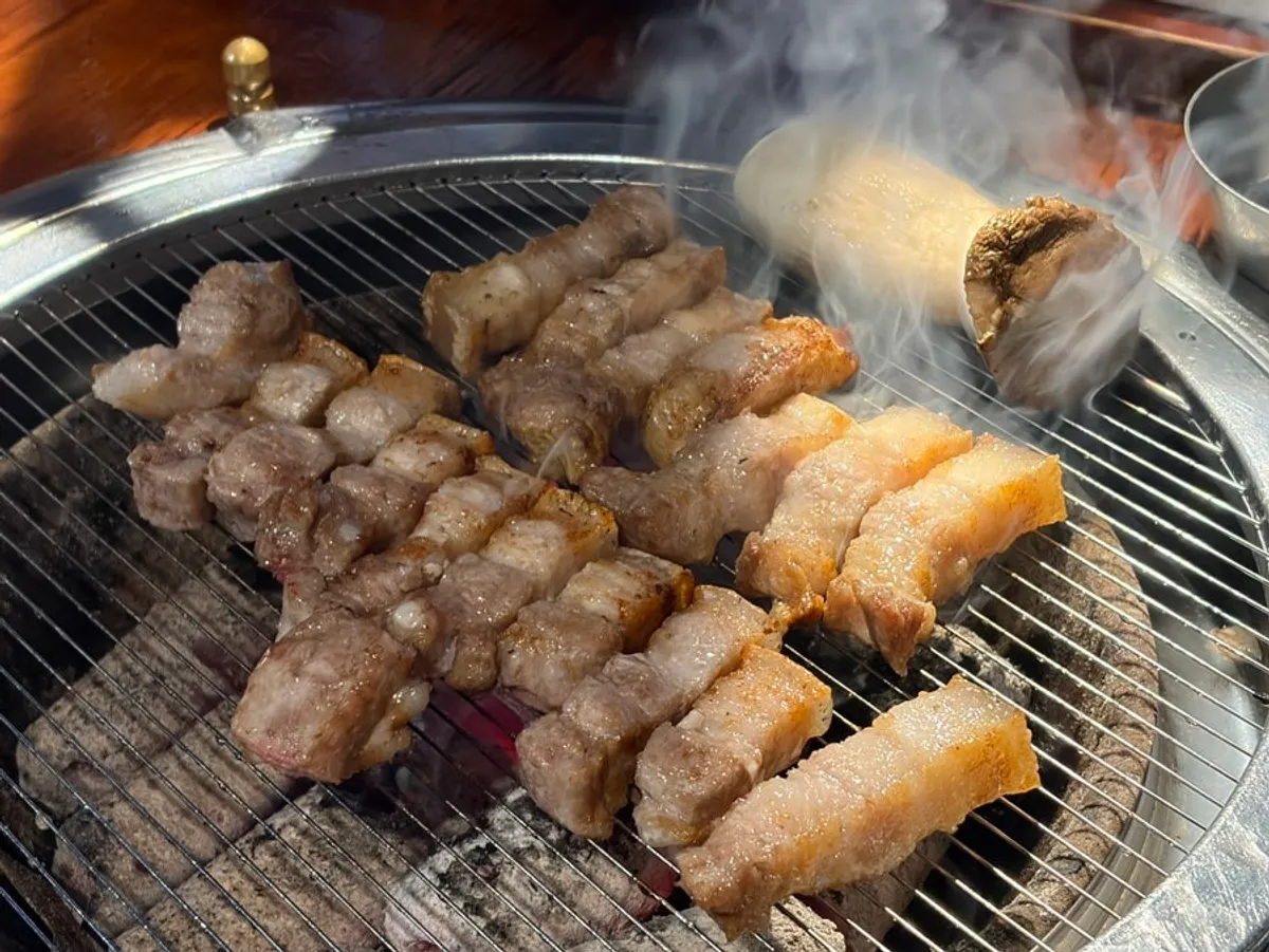 Golden-brown grilled yukgyeopsal and ogyeopsal on the grill pan at Yuk Tongryeong