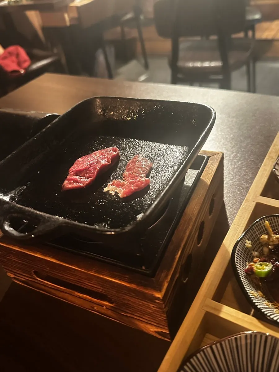Mini charcoal grill brought to the table with meat searing on it