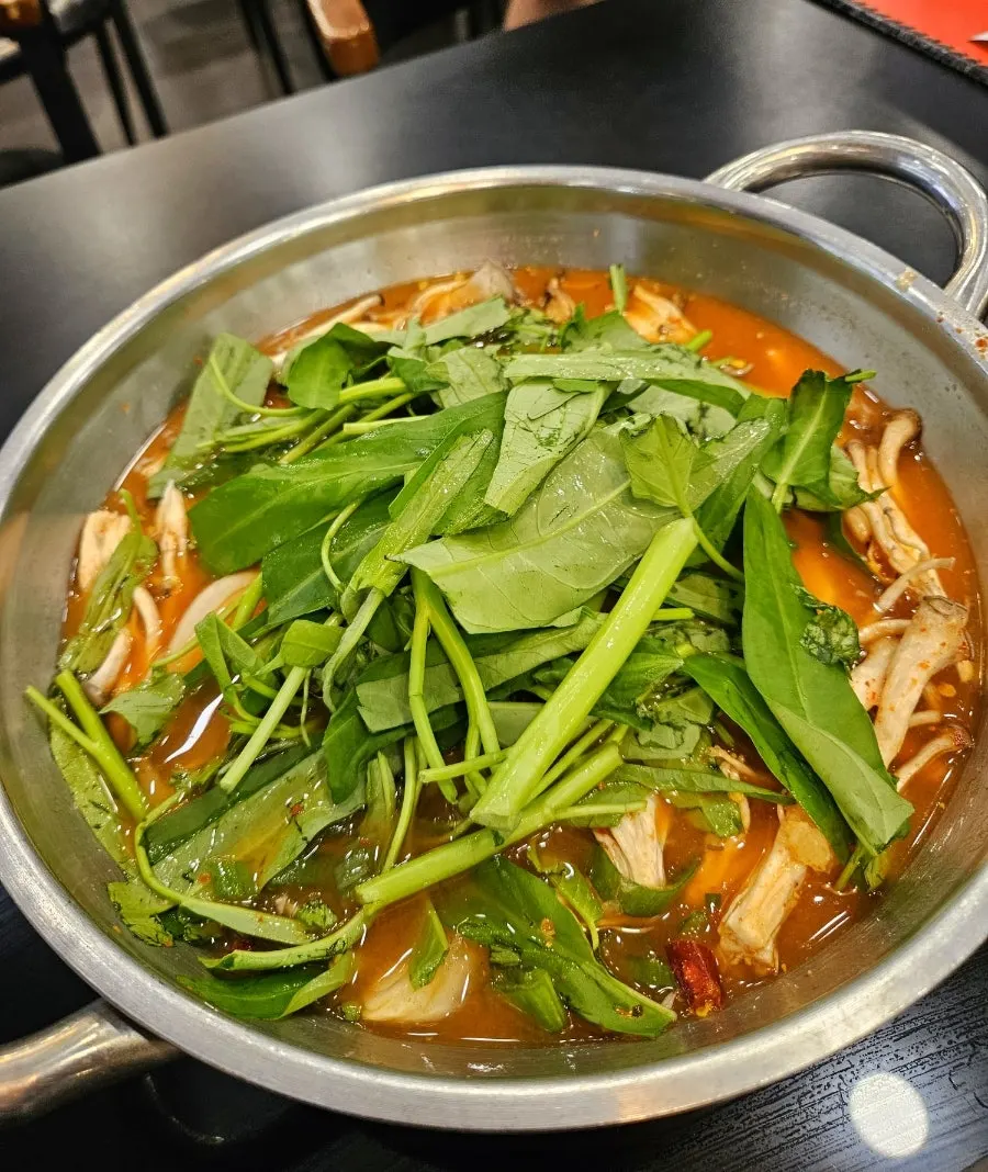 Pot of bubbling red broth with vegetables and mushrooms