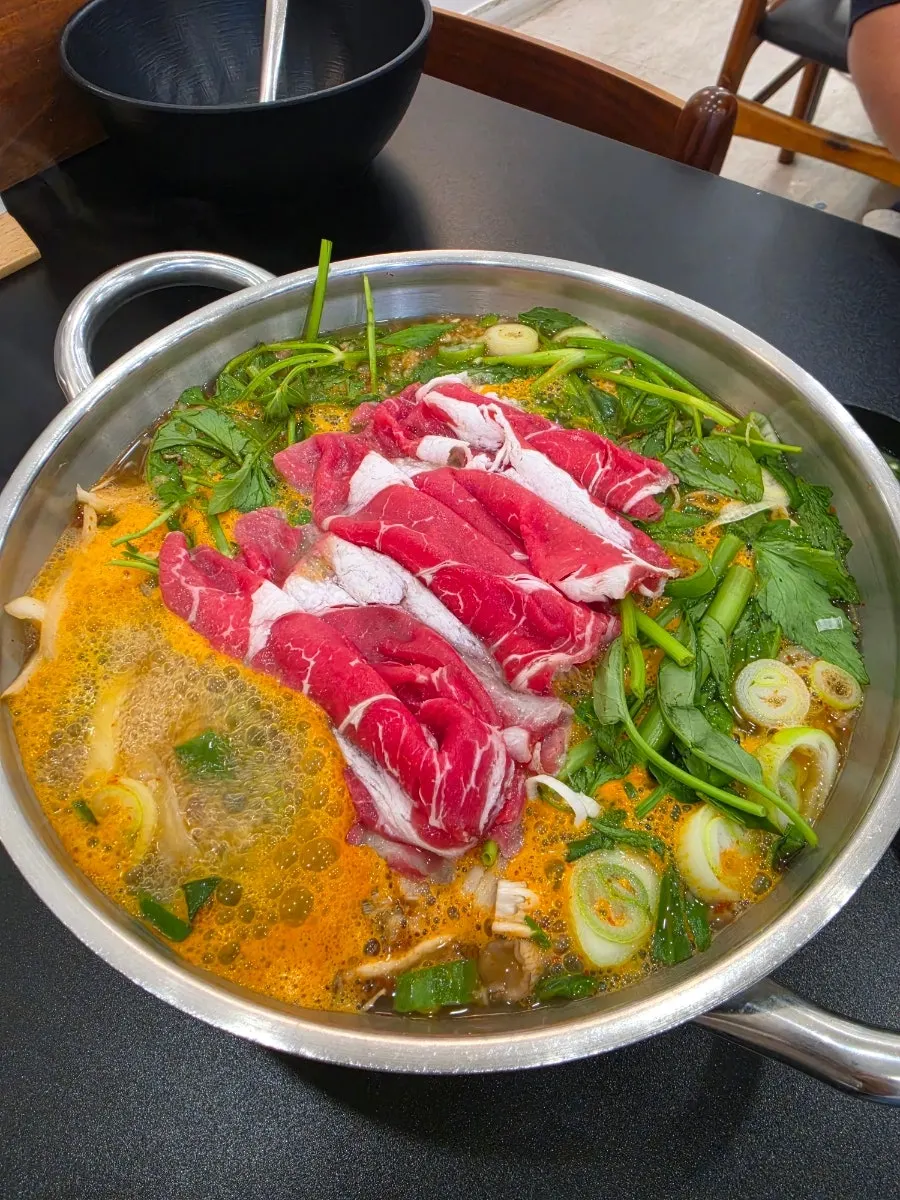 Pot of red broth simmering with half the meat added